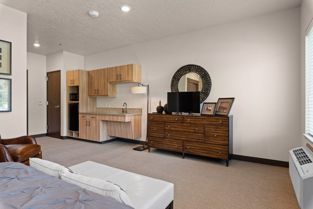 A modern room featuring a dresser with a television and mirror above, as well as a small kitchenette area.