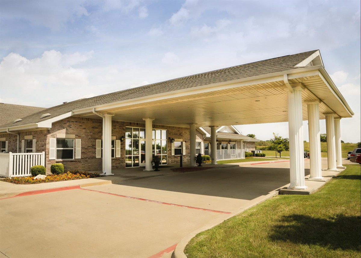 A building with a large covered entrance supported by columns, surrounded by landscaped areas.