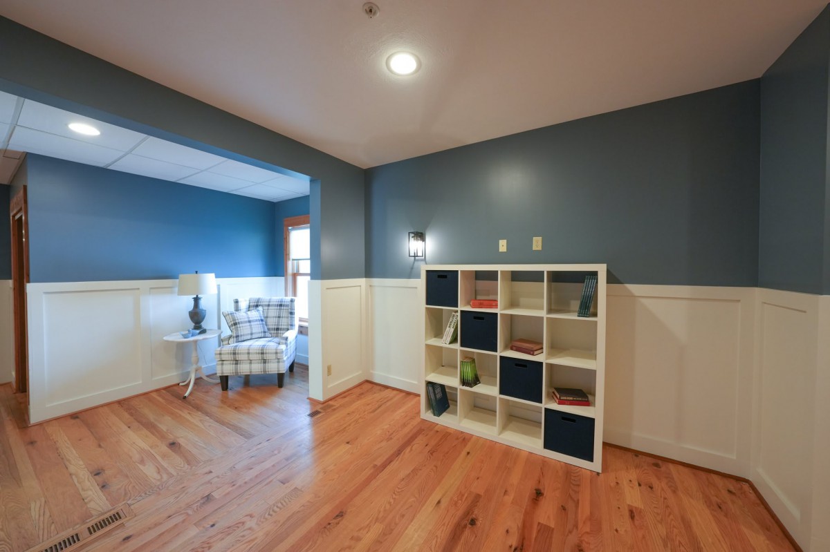 A modern room with wood flooring and blue walls, featuring a white shelving unit and stylish decor.