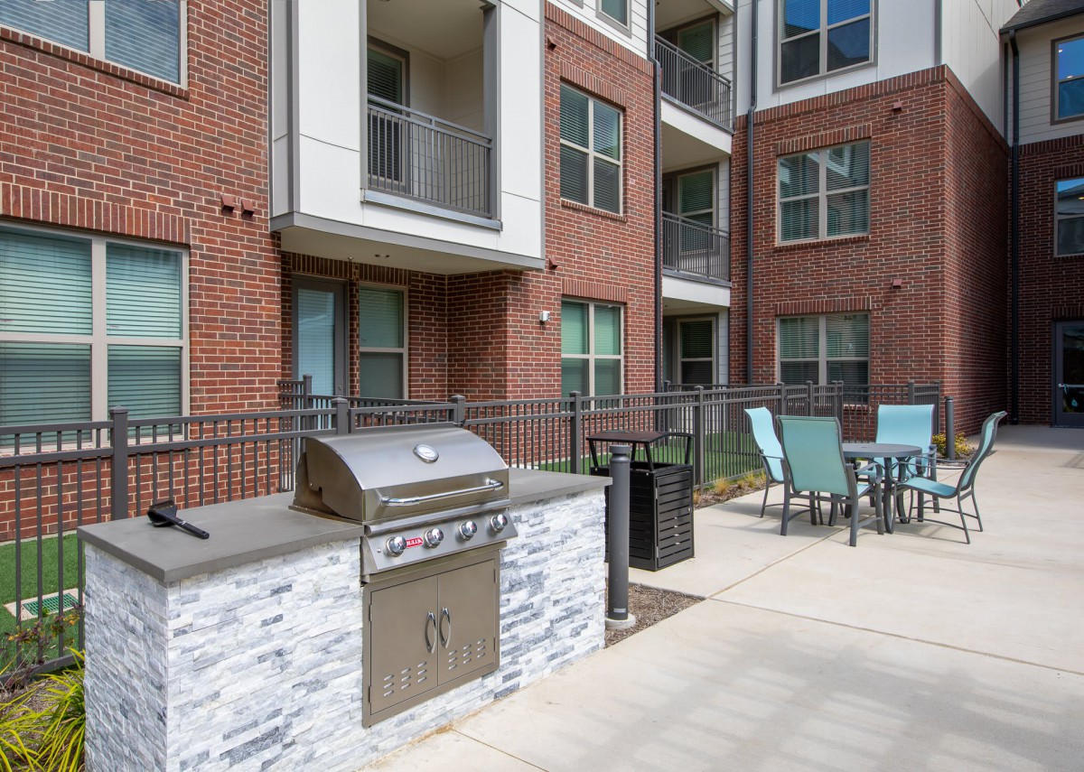 An outdoor patio area at an apartment complex, featuring a grill and seating.