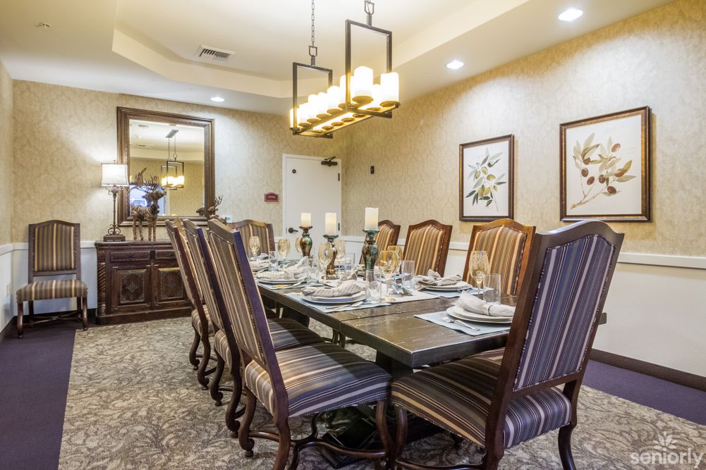 An elegantly designed dining room with a large table, set for a meal, surrounded by ornate chairs and illuminated by a chandelier.