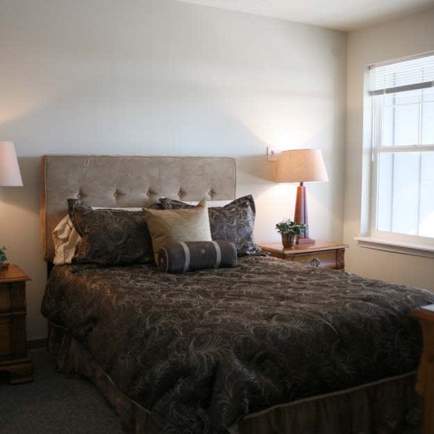 A cozy bedroom with a large bed, nightstands, and two lamps situated near a window.