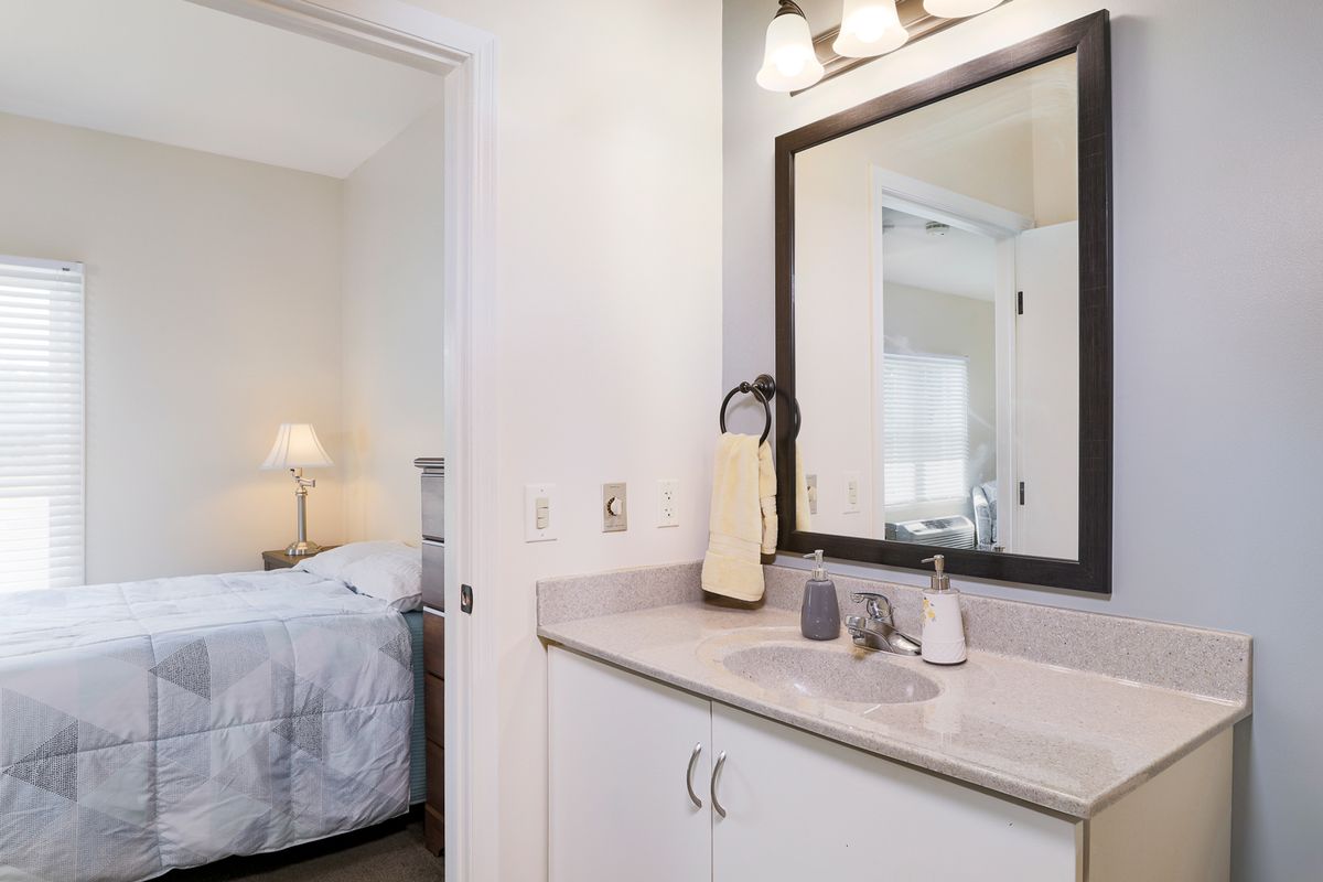 A well-lit bathroom with a mirror and sink, connected to a cozy bedroom.
