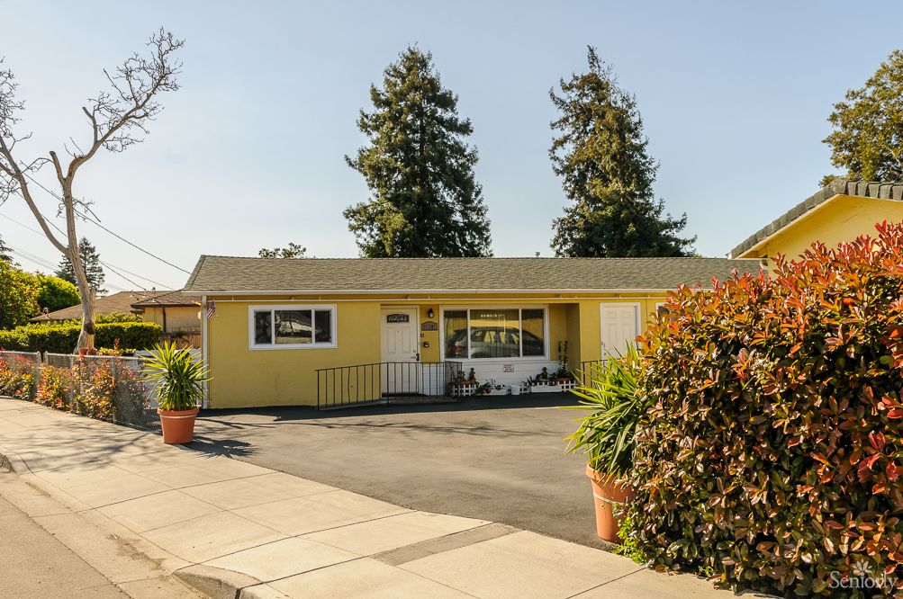 A yellow suburban house with a driveway and surrounding trees.