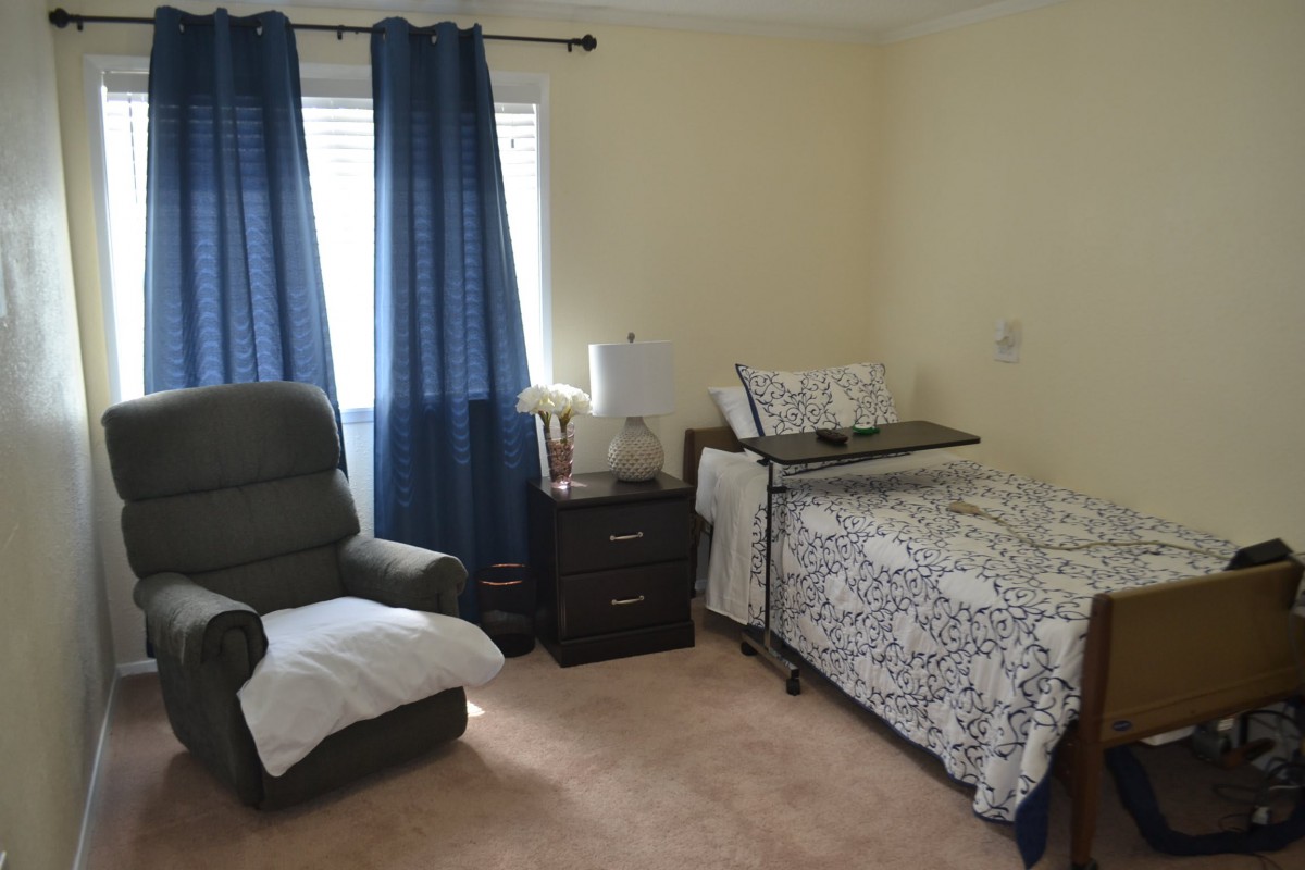 A cozy bedroom with a single bed, an armchair, a nightstand, and blue curtains.