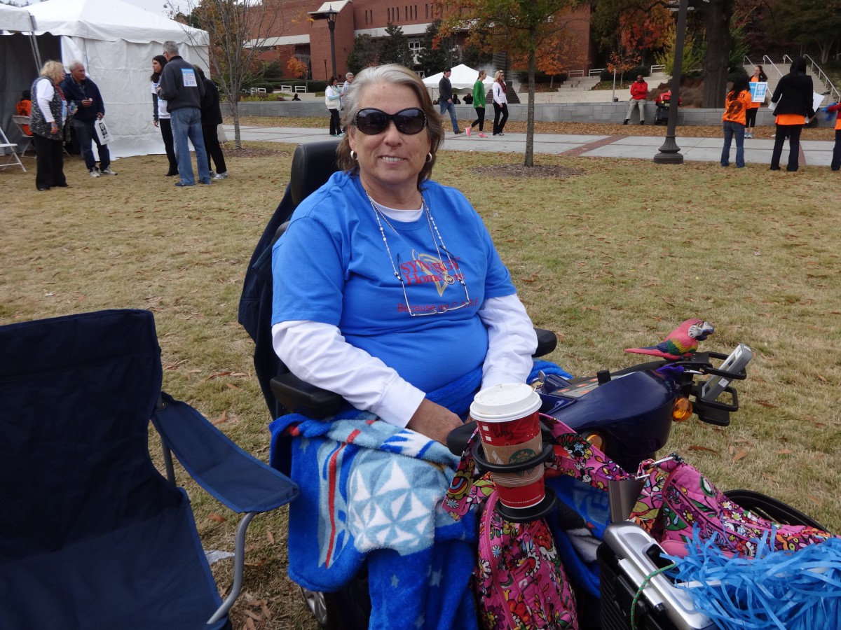 A person enjoying a festival outdoors in a wheelchair, wearing sunglasses and a t-shirt.