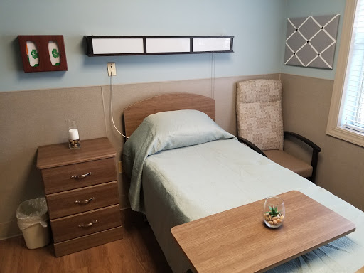 A cozy hospital room featuring a single bed, bedside table, and comfortable chair.