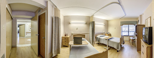 A well-lit hospital patient room featuring two beds, storage furniture, and curtains for privacy.