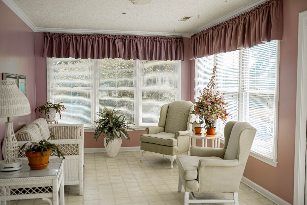 A cozy sunroom with large windows, elegant chairs, and potted plants.
