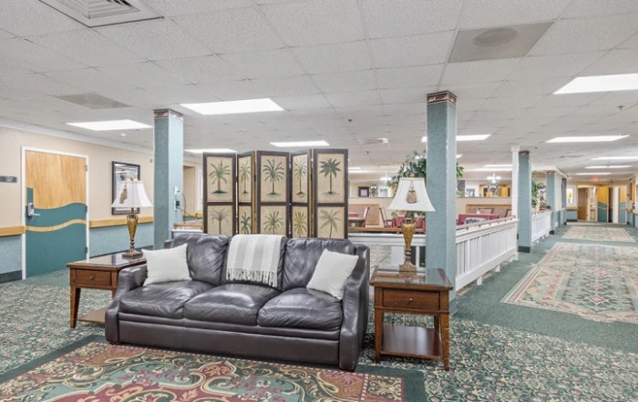 A cozy lobby area featuring a leather sofa, wooden end tables with lamps, and decorative elements including a room divider and patterned carpet.