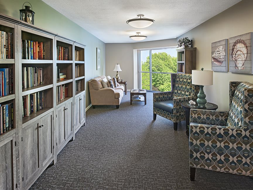 A cozy living room with bookshelves, seating area, and a large window offering natural light.