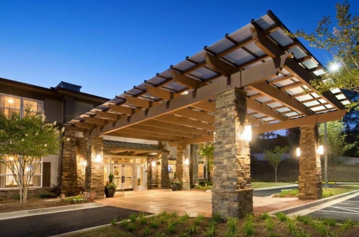A well-lit building entrance with stone pillars and a wooden roof structure during the evening.