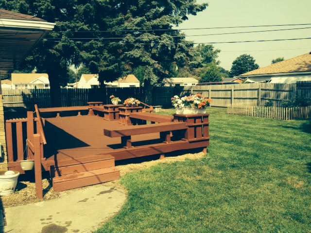 A sunny backyard with a wooden deck and surrounding lawn.