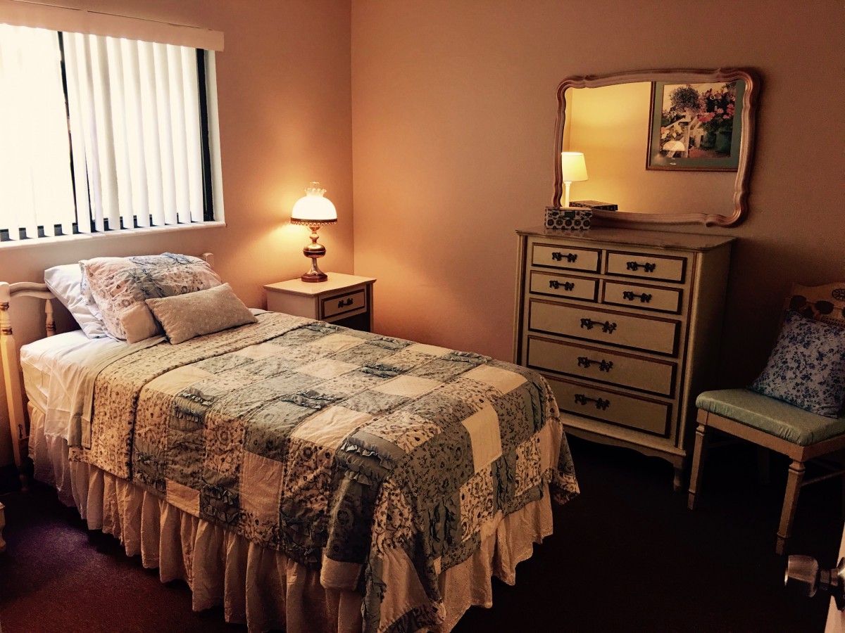 A cozy bedroom with a bed, nightstand, dresser, and warm lighting.
