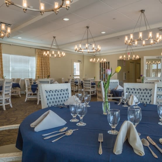 An elegant dining room with tables set for guests, featuring blue tablecloths and ambient chandelier lighting.
