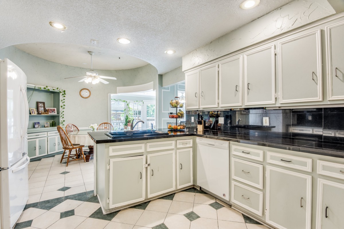 A spacious kitchen with white cabinets and a black countertop, leading to a cozy dining area.
