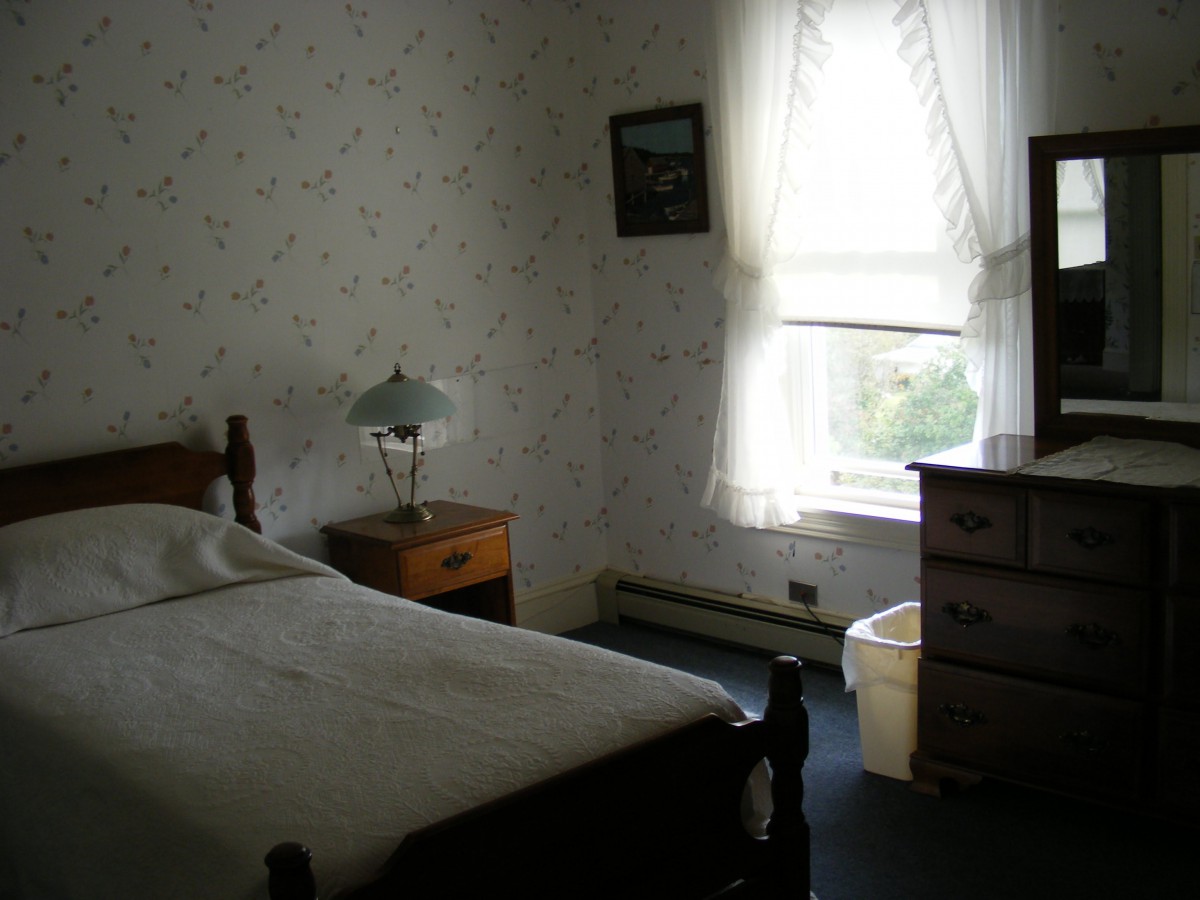 A cozy vintage bedroom with a single bed, nightstand, lamp, and dresser.