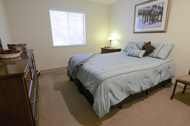 A cozy bedroom with a neatly made bed, bedside lamp, and wall art.