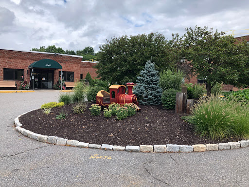 A colorful garden featuring a decorative train, surrounded by various plants and flowers at the entrance of a building.