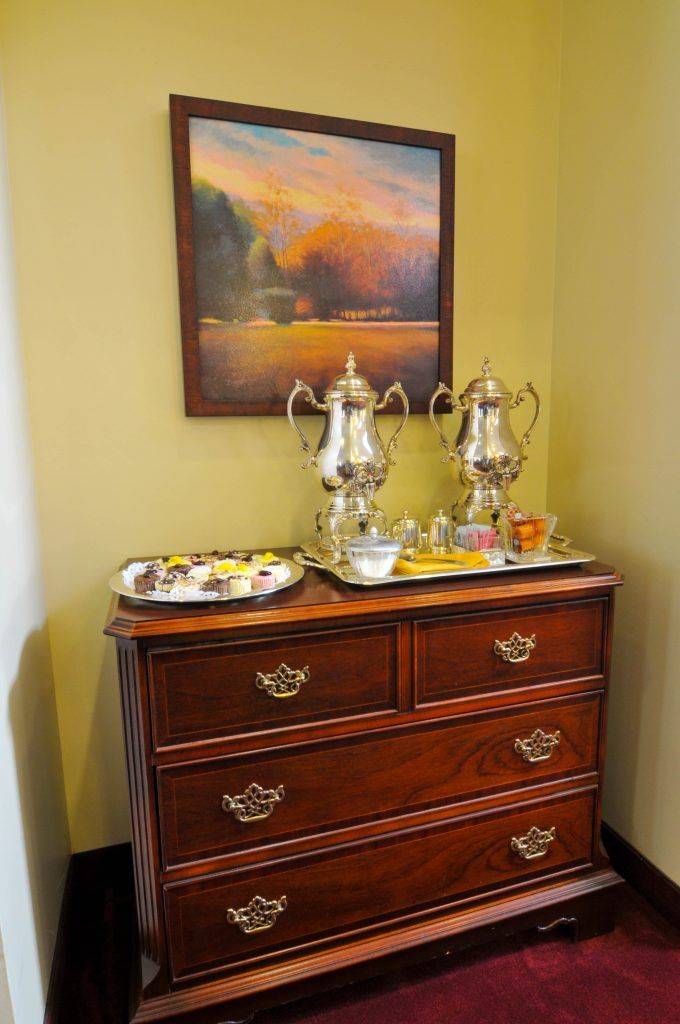 A classic wooden dresser topped with silver teapots and cups, featuring a decorative tray and a framed painting above.