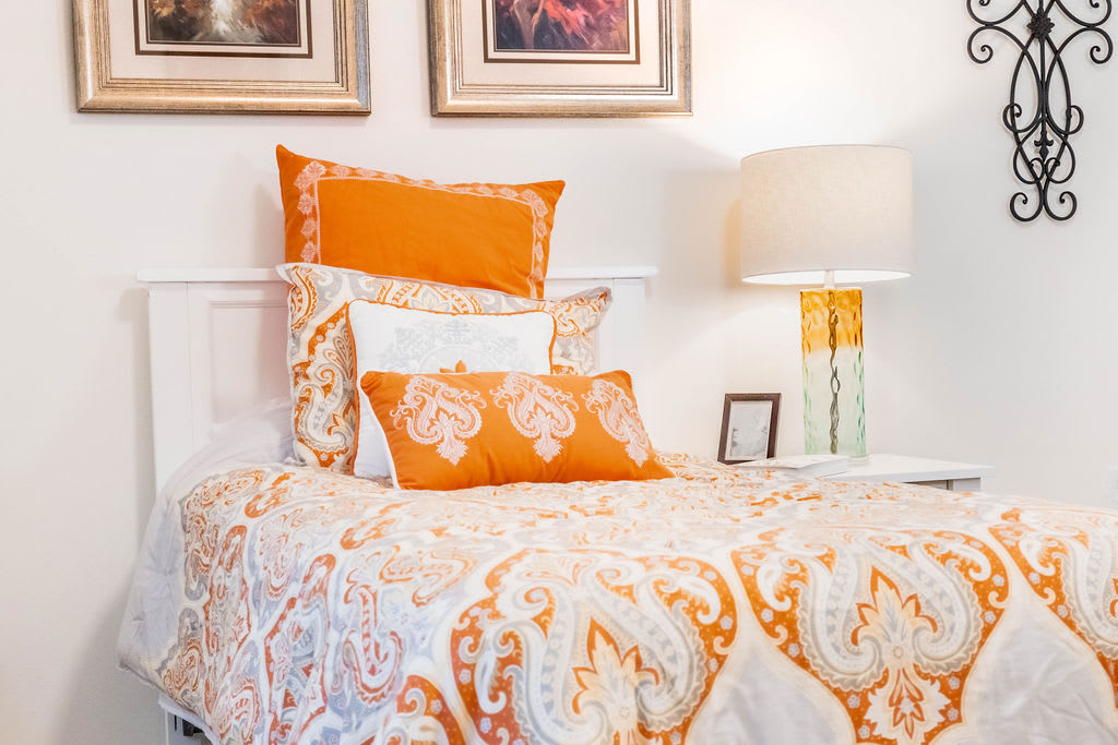 A cozy bedroom with orange and white patterned bedding, complemented by matching pillows and a bedside lamp.