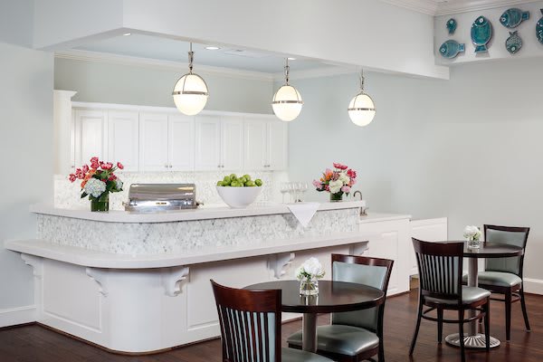 A modern kitchen with a marble countertop, pendant lights, and dining area featuring wooden chairs and a round table.