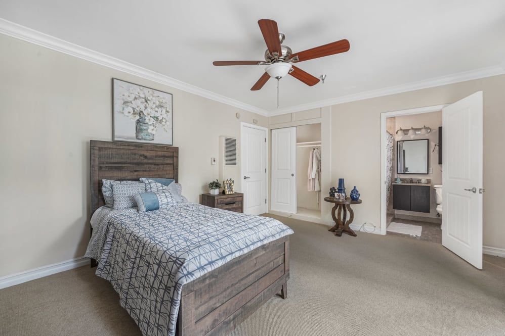 A modern bedroom with a wooden bed frame, ceiling fan, and neutral decor.