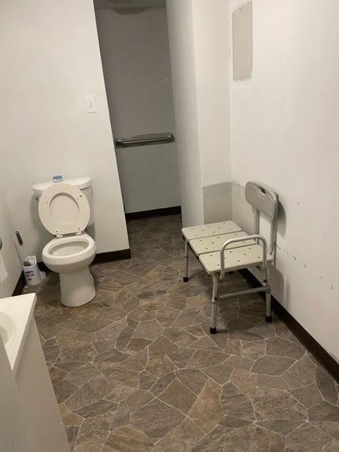 A simple bathroom setup with a toilet and a chair against white walls.