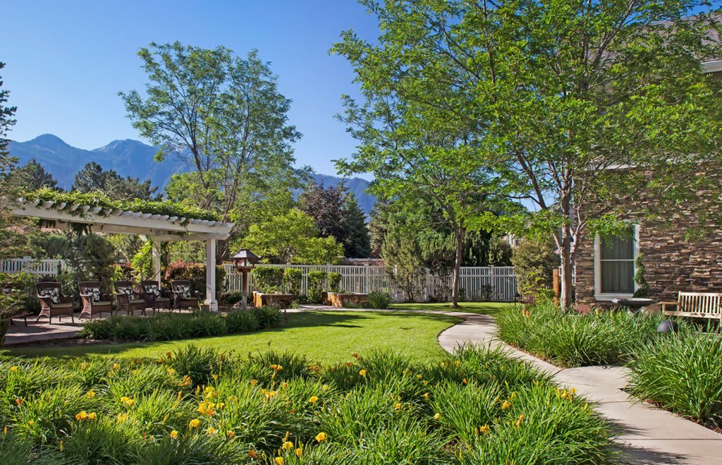 A beautifully landscaped garden with a lush lawn, trees, and a pathway under a clear blue sky.