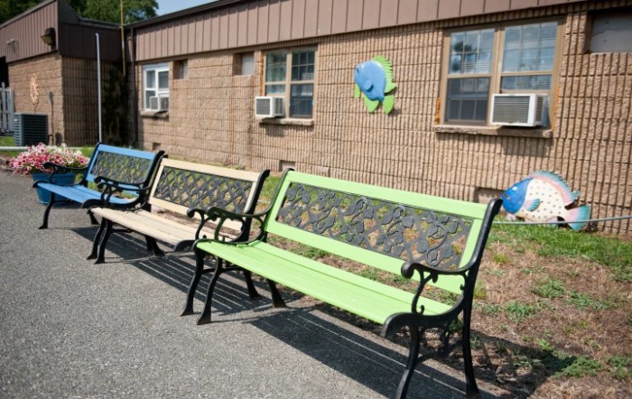 Outdoor benches placed against a brick building with windows and air conditioners.