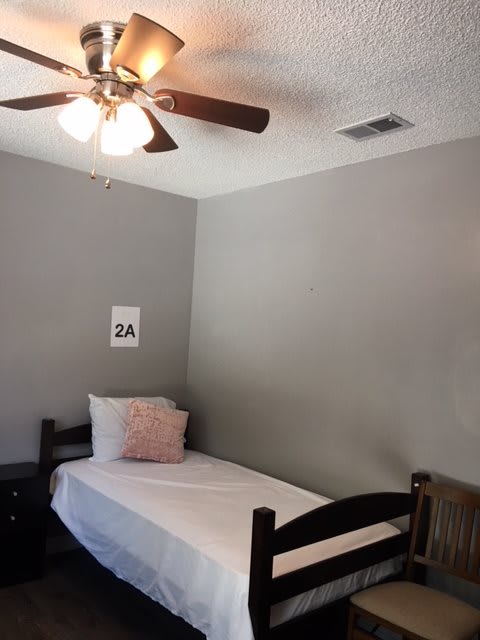 A minimalist bedroom featuring a single bed with a pink pillow and a ceiling fan.