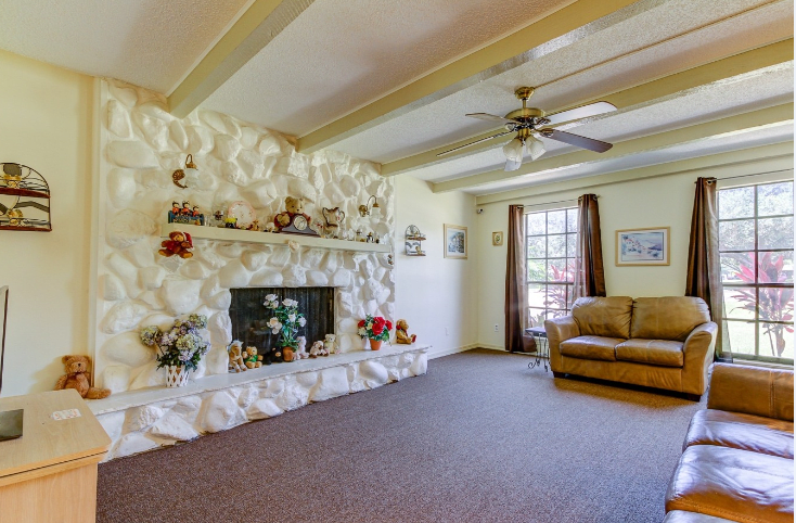 A cozy living room featuring a textured fireplace, comfortable couch, and large window with curtains.