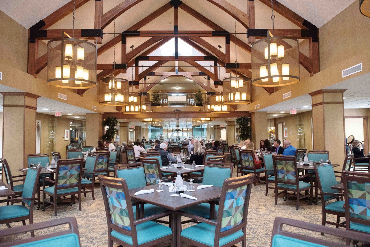 A spacious restaurant interior featuring wooden ceiling beams and elegant lighting, with neatly arranged tables and chairs.