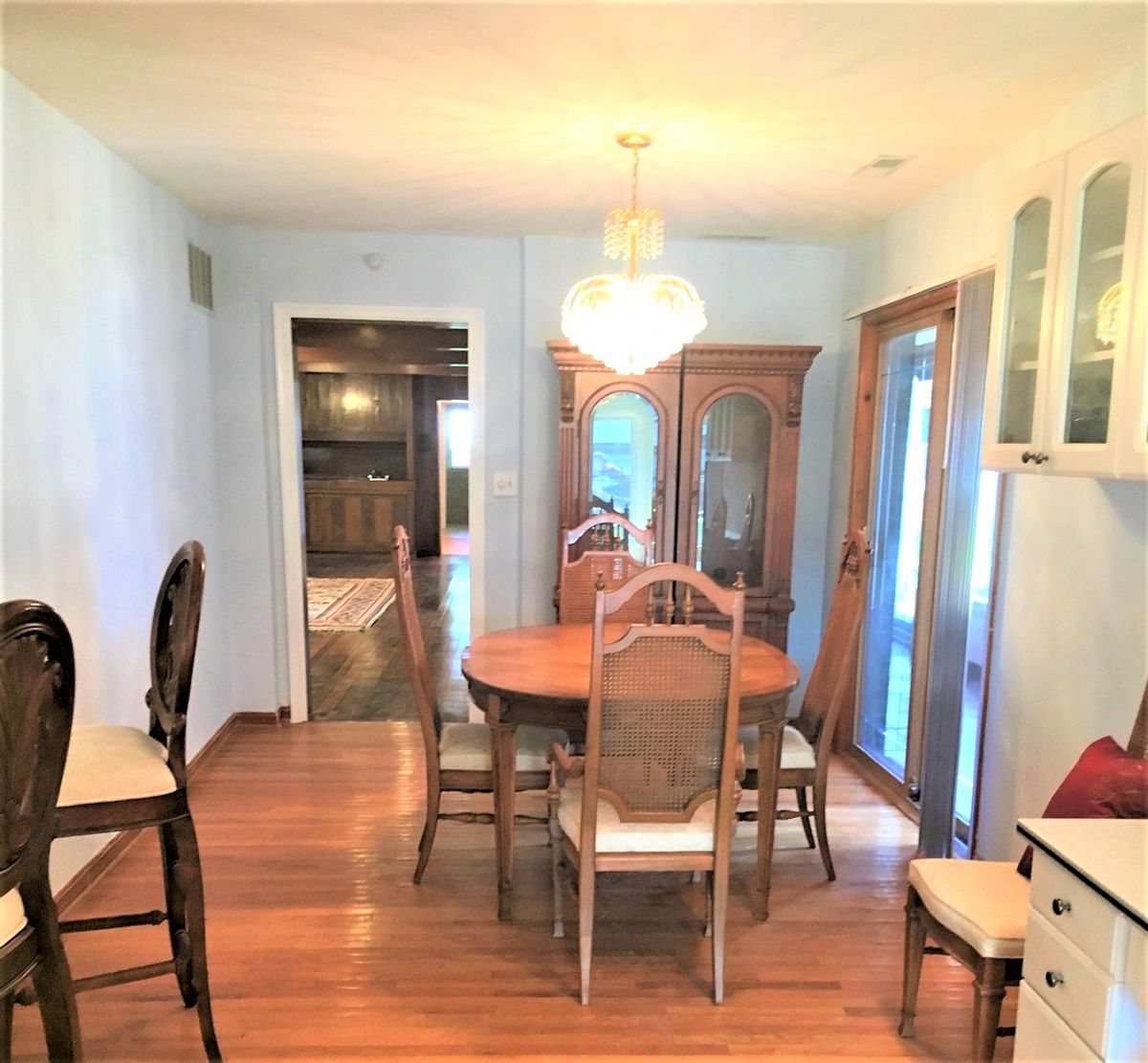 A cozy dining room featuring a wooden table, chairs, and a cabinet with a chandelier overhead.