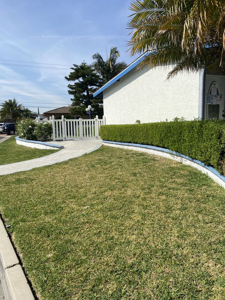 A well-maintained yard with a sidewalk leading to a white fence and house.
