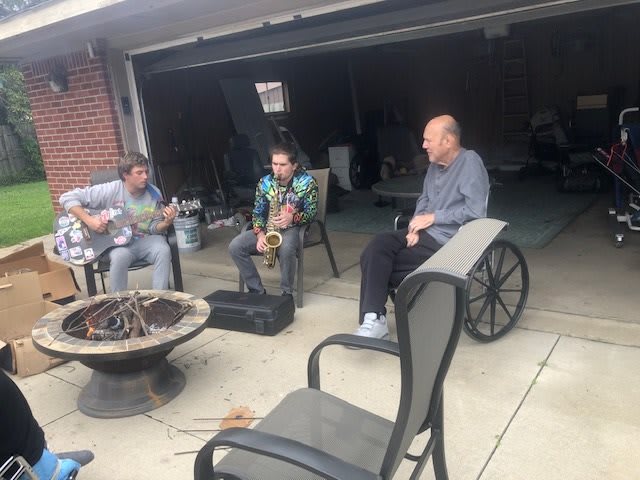 A casual music session in a driveway with friends playing instruments.