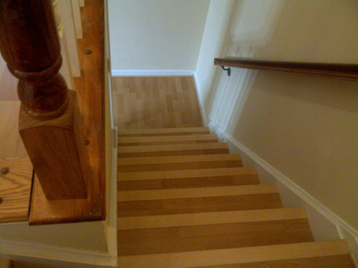 A view of wooden stairs leading down with a handrail on the right side.