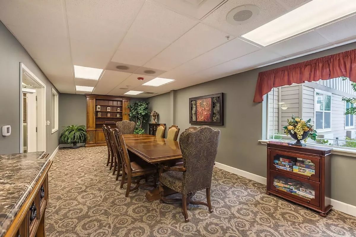 A well-furnished conference room with a large table and chairs, featuring a bookshelf, indoor plants, and decorative artwork.