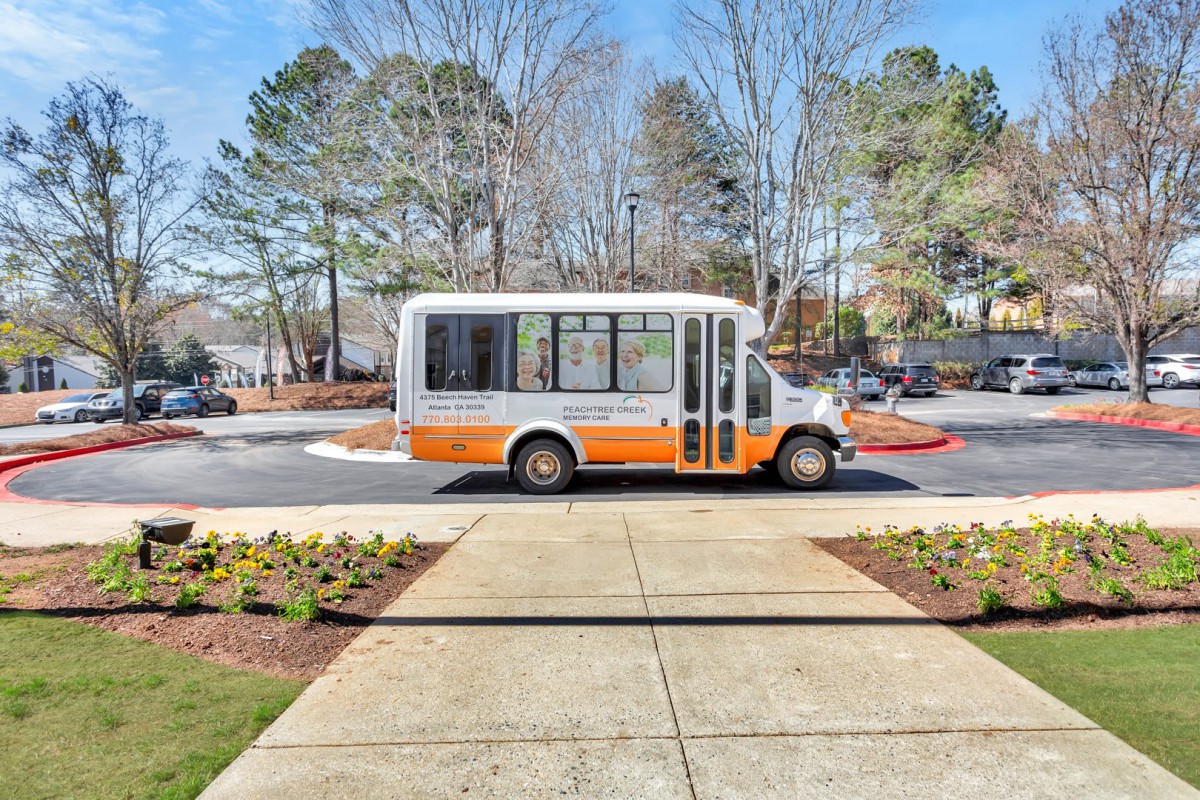 A small bus is parked on a road next to a sidewalk, surrounded by trees.