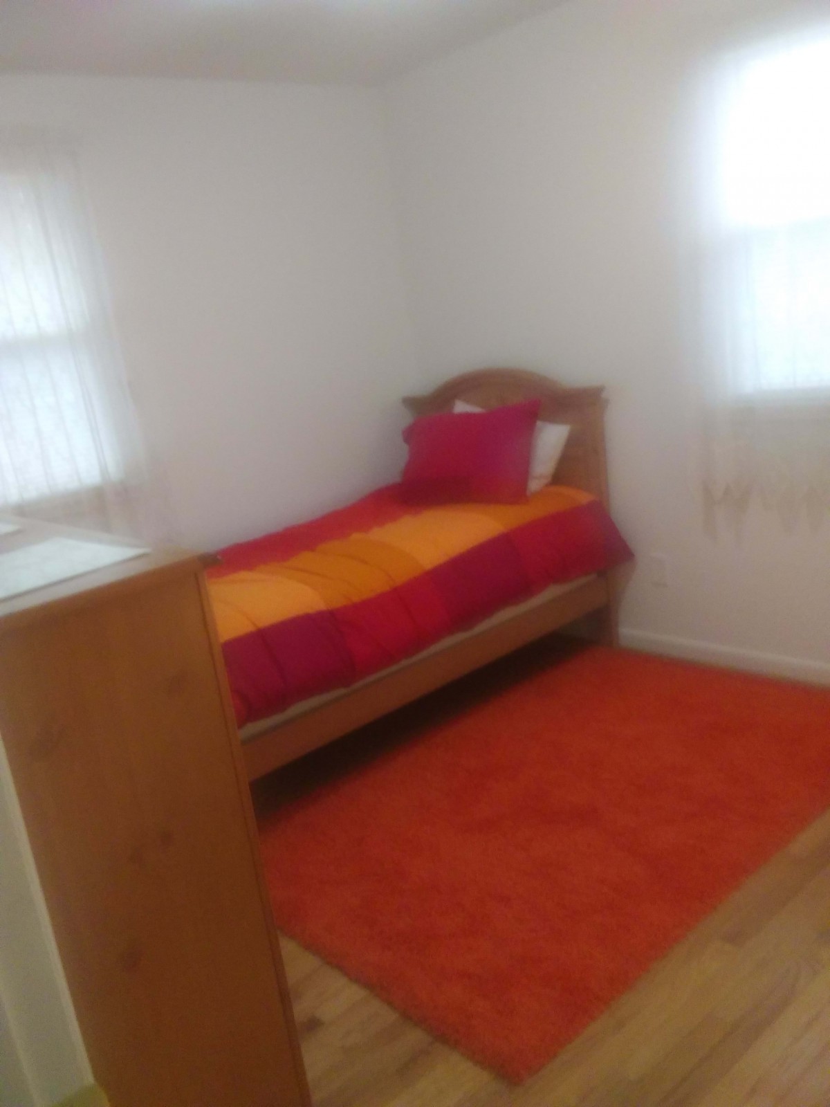 A minimalist bedroom featuring a single bed with colorful bedding and an orange rug.