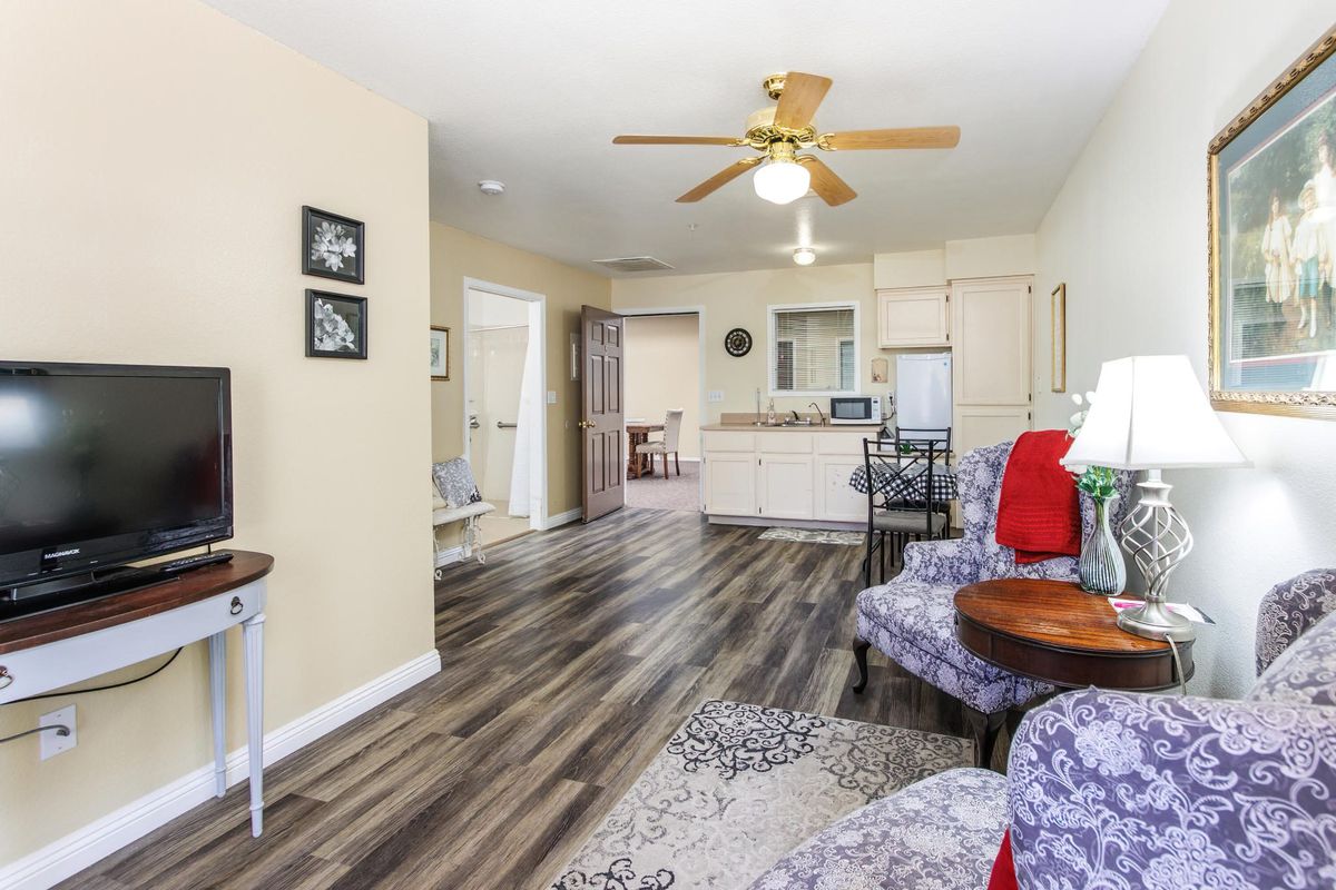 A cozy living room with hardwood floors, a ceiling fan, and an open view into the kitchen.