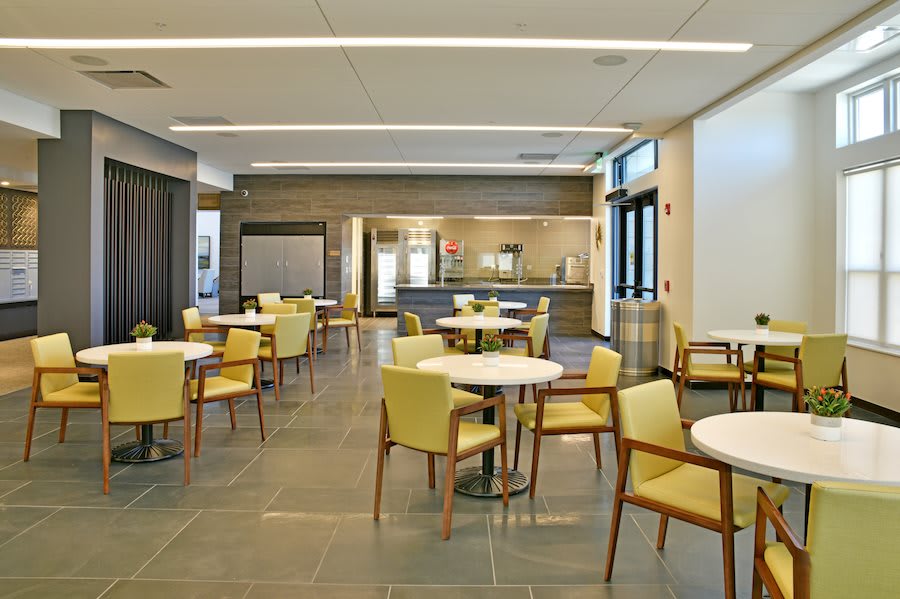 A modern, empty cafeteria with yellow chairs and round tables.