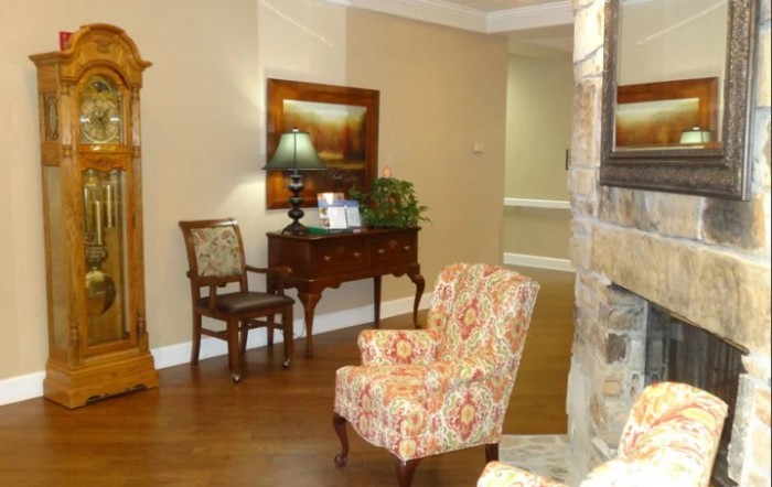 A cozy living room with a patterned armchair, wooden furniture, a lamp, and decorative elements.
