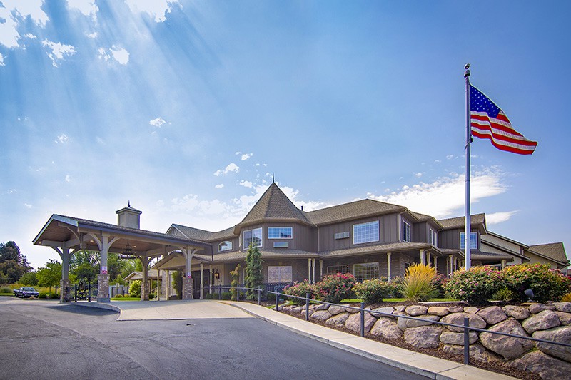 A large, multi-story building with a driveway in front and a flagpole, set against a clear blue sky.