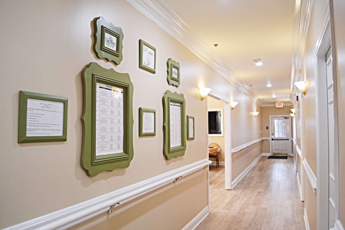 A well-lit hallway featuring decorative frames on the walls and a warm wooden floor.