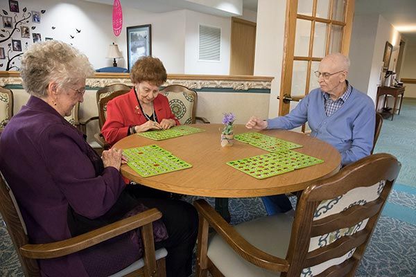 A group of elderly people playing bingo around a table in a community setting.