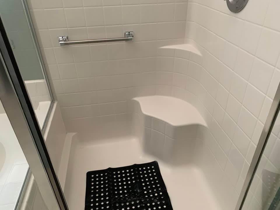 A bathroom shower with a built-in seat, towel rack, and floor mat.
