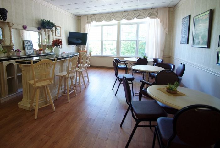 A cozy cafe interior with tables and chairs, featuring a bar counter and large windows allowing natural light to brighten the space.