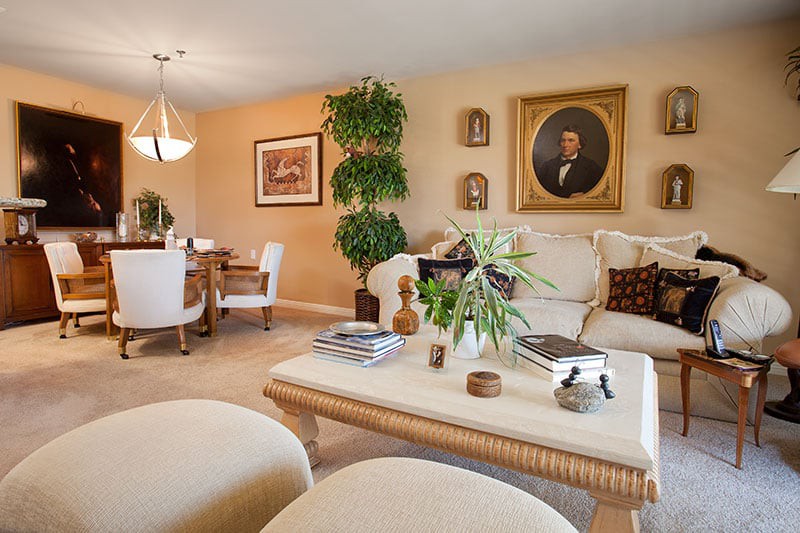 A cozy living room with a neutral color scheme, featuring comfortable seating, a coffee table adorned with decorative items, and a dining area in the background.