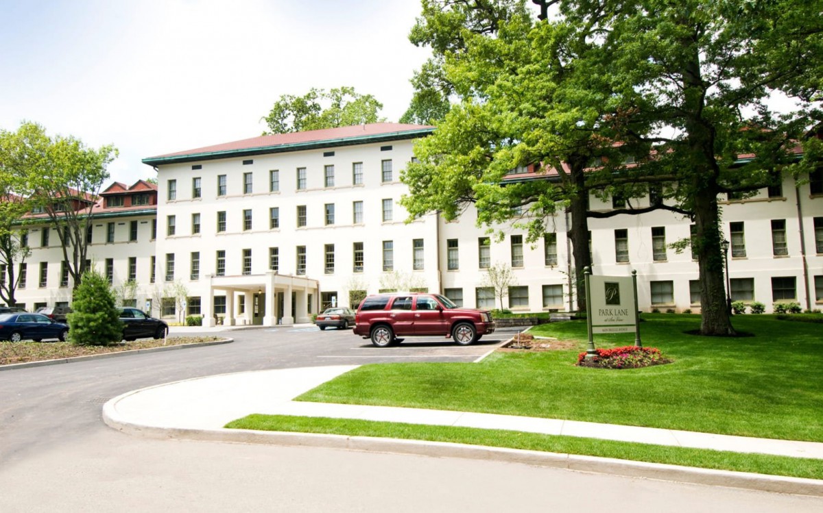 A multi-story building surrounded by trees and parked cars, with a neatly maintained lawn in the foreground.